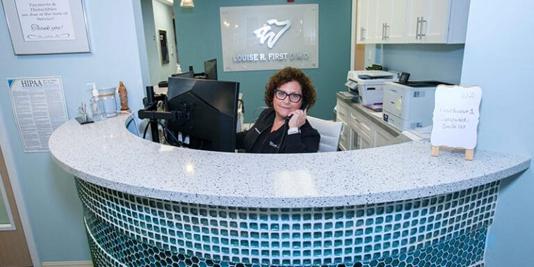 Receptionist answering a phone call at a curved front desk inside a dental office