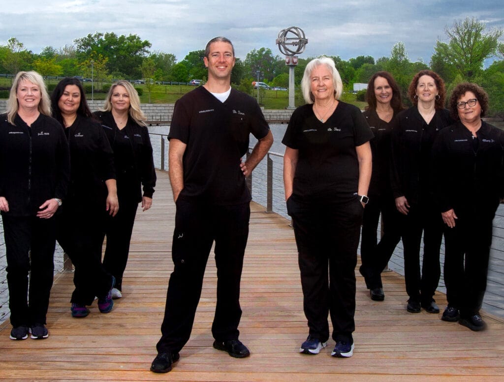 Smiles by Choice dental team standing on a boardwalk near a body of water, smiling and wearing matching black uniforms