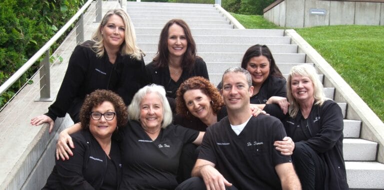Dental team sitting together on outdoor stairs, smiling at the camera