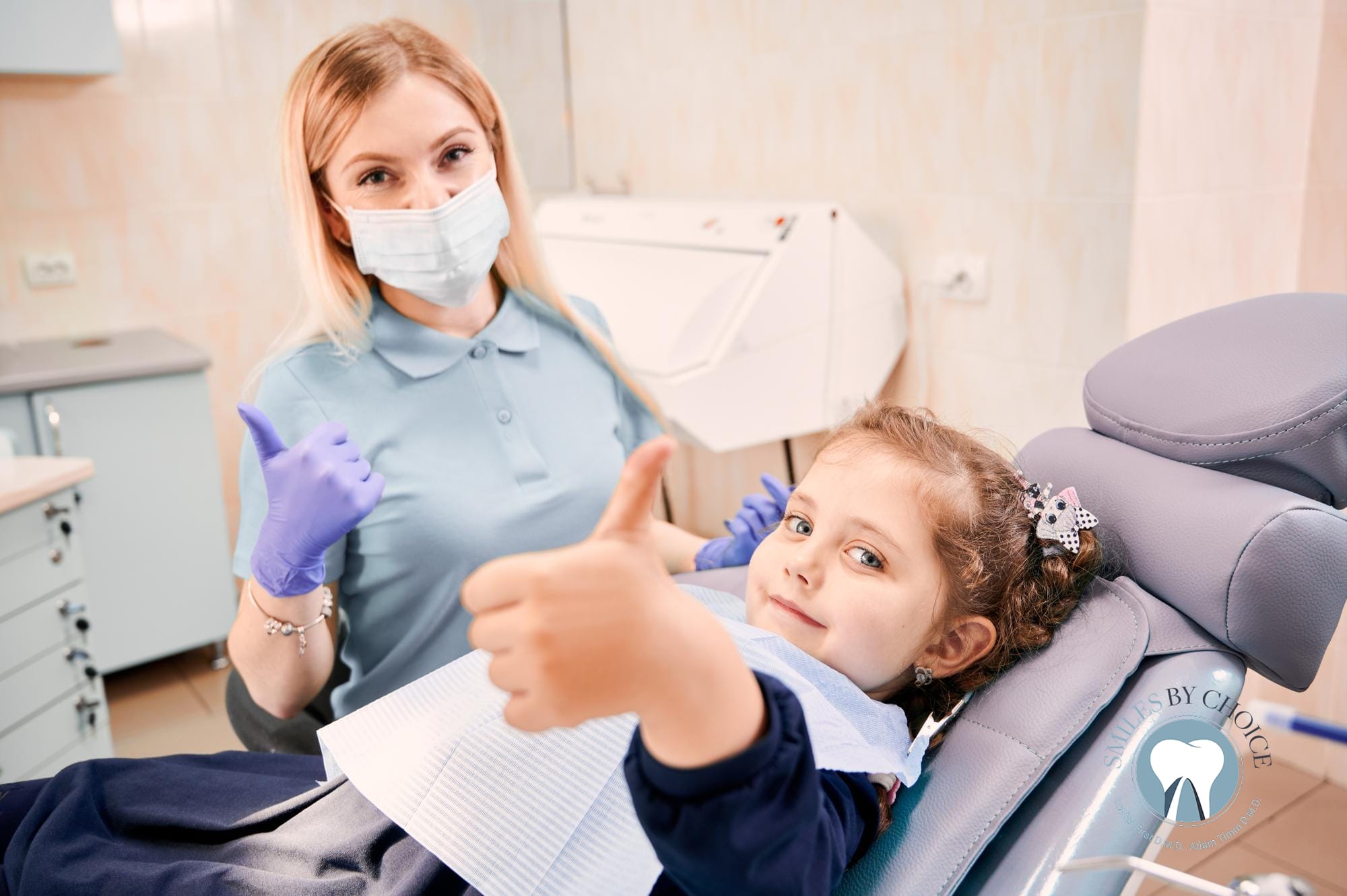 Female pediatric dentist and young girl giving a thumbs up during a comfortable dental checkup