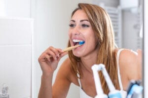 Woman brushing her teeth while looking in the mirror as part of daily oral care routine.