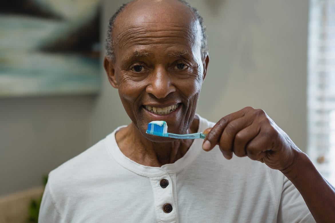 Senior Black man smiling and holding a toothbrush in hand, promoting dental hygiene